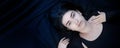 Wide banner panorama portrait of black haired young lying woman with beguiling hypnotic look on blue black fabric background, Royalty Free Stock Photo