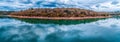 Panorama of trees growing on lakeshore with scenic clouds reflections.