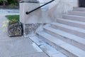 Wide concrete entry stairs on a church exterior, black metal pipe railing and stone planter alongside a concrete sidewalk