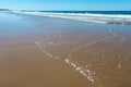 Wide expanse of wet beach with water retreating and low waves coming in and foam and water on the beach and reflection of turqoise