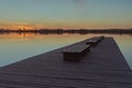 A wide and long wooden jetty with benches, sunset and calm lake