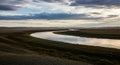 A wide, meandering river flows through expansive grasslands under a cloudy sky. The Royalty Free Stock Photo