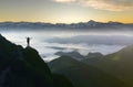 Wide mountain panorama. Small silhouette of tourist with backpack on rocky mountain slope with raised hands over valley covered