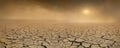 Wide panorama of barren cracked land with sun barely visible through the dust storm. Drought and desertification concept