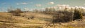 wide panoramic view of the early spring or late autumn hilly field with dry grass on the slopes, bare trees and a rural road under Royalty Free Stock Photo