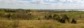 wide panoramic view of a hilly field with wild grass and trees, farmland, forest belts and a lake on a spring day under a blue Royalty Free Stock Photo