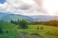 Wide peaceful summer landscape. Empty field road stretching to horizon through green grassy meadow and trees lit by sun towards Royalty Free Stock Photo