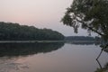 Wide river flowing across green forest. Fall. Evening. Reflections of trees in the calm water. Sundown Royalty Free Stock Photo