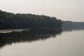 Wide river flowing across green forest. Fall. Evening. Reflections of trees in the calm water. Sundown Royalty Free Stock Photo