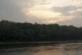 Wide river flowing across green forest. Fall. Evening. Reflections of trees in the calm water. Sundown Royalty Free Stock Photo