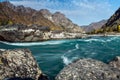 Wide river flows along stony banks among rocky mountains against clear blue sky. Turquoise water of stormy river and huge stones. Royalty Free Stock Photo