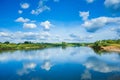 Wide river with reflection and green bush on coasts and blue cloudy sky Royalty Free Stock Photo