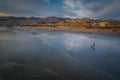 Wide sandy beach with people, Pacific ocean, hills, and cloudy sky. Pismo Beach at sunset, California coastline