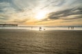 Wide sandy beach at sunset. Walking people, wooden pier, seashore, and sun setting down the horizon, Pismo Beach, California Royalty Free Stock Photo