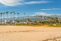 Wide sandy Santa Barbara beach with beautiful palm trees, city architecture in silhouette, mountains, and cloudy sky on background Royalty Free Stock Photo