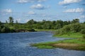 A wide shallow river flows in a field with trees