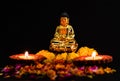 Wide shot of buddha statue with two glowing clay lamps and flowers on black background. buddhism concept