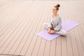 Wide shot of calm young woman sitting on yoga mat with closed eyes and meditating in butterfly pose, tilting head Royalty Free Stock Photo