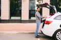 Wide shot of delivery man standing near car, large festive white box with beautiful red bow at truck Royalty Free Stock Photo