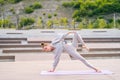 Wide shot of flexible young yogini woman doing yoga standing on fitness mat on summer day outdoors. Royalty Free Stock Photo