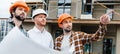 wide shot of group of architects with building plan standing in front of construction site