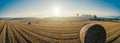 Wide shot of hay bale on golden sunlit farm field with clear blue sky and trees in the background. Horizontal shot