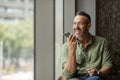 Wide shot mature man with beard talking on phone next to sunny window Royalty Free Stock Photo