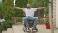 Wide shot portrait of smiling cheerful paraplegic man in wheelchair with stretched hands on sunny day outdoors. Happy