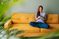 Wide shot portrait of upset young woman using phone, sitting alone on sofa at home, receiving, reading bad news, message Royalty Free Stock Photo