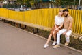 Wide shot of pretty young couple in love resting in city park sitting hugging with closed eyes on bench in summer day Royalty Free Stock Photo