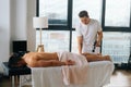 Wide shot of professional male masseur massaging leg calf muscles using massage gun percussion tool of muscular athlete Royalty Free Stock Photo