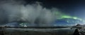 Wide shot of a sea and the shore under the clouds and the northern lights in the sky