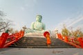 Wide shot and side view of young Asian monk hold red umbrella and walk down on stair in front of green big buddha statue with soft