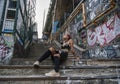 Wide shot of Street punk girl in Urban. Girl Sitting on the Stairs painted with graffiti under the Bridge