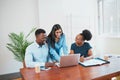 Wide shot of three colleagues smiling and looking at laptop in boardroom