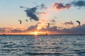 Wide shot of three kitesurfers riding in sunset conditions with colorful clouds in the sky