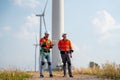 Wide shot of two Caucasian engineers or technicians stay in front of cluster of windmill or wind turbine for maintenance or manage