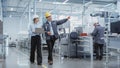 Wide Shot: Two Heavy Industry Employees in Hard Hats Discussing Job Assignments at the Factory