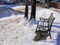 Wide shot of a wrought iron bench with the seat covered in snow on a beautiful pondside on a cold winter morning