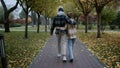 Wide shot of young happy lovers walking in autumn park on cloudy weather. Royalty Free Stock Photo