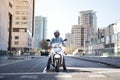 Wide shot of a young motorcyclist stopped at a traffic light in Barcelona. The man riding his scooter through