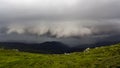 Wide summer mountain panorama before thunderstorm. Dark rain clouds low over green grassy rocky valley and distant mountain range