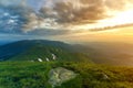 Wide summer mountain view at sunrise. Glowing orange sun raising in blue cloudy sky over green grassy hill soft grass and distant Royalty Free Stock Photo