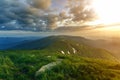 Wide summer mountain view at sunrise. Glowing orange sun raising in blue cloudy sky over green grassy hill soft grass and distant Royalty Free Stock Photo