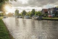 Wide tree-lined canal with houses and boats and shine of sunset reflected in water at Weesp. Royalty Free Stock Photo