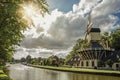 Wide tree-lined canal with windmill and boats and shine of sunset reflected in water at Weesp. Royalty Free Stock Photo