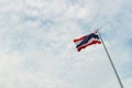 A wide, up-tilt shot of a Thai flag that is hit and moved by the wind on the top of a pole with clear sky background