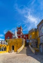 Wide view of the arched courtyard with stone stairs and the yellow and red painted walls of the Pena Palace, with a rock Royalty Free Stock Photo