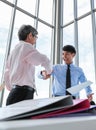 Wide view shot of two Asian businessmen looking at each other eyes with a pleasant smiling and shaking hands. The senior and young