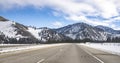 Wide winter highway heading into snow-capped mountains with snow-covered roadsides and fields in Montana Royalty Free Stock Photo